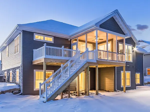 An elevated, large deck attached to a house with slate gray siding covered in snow