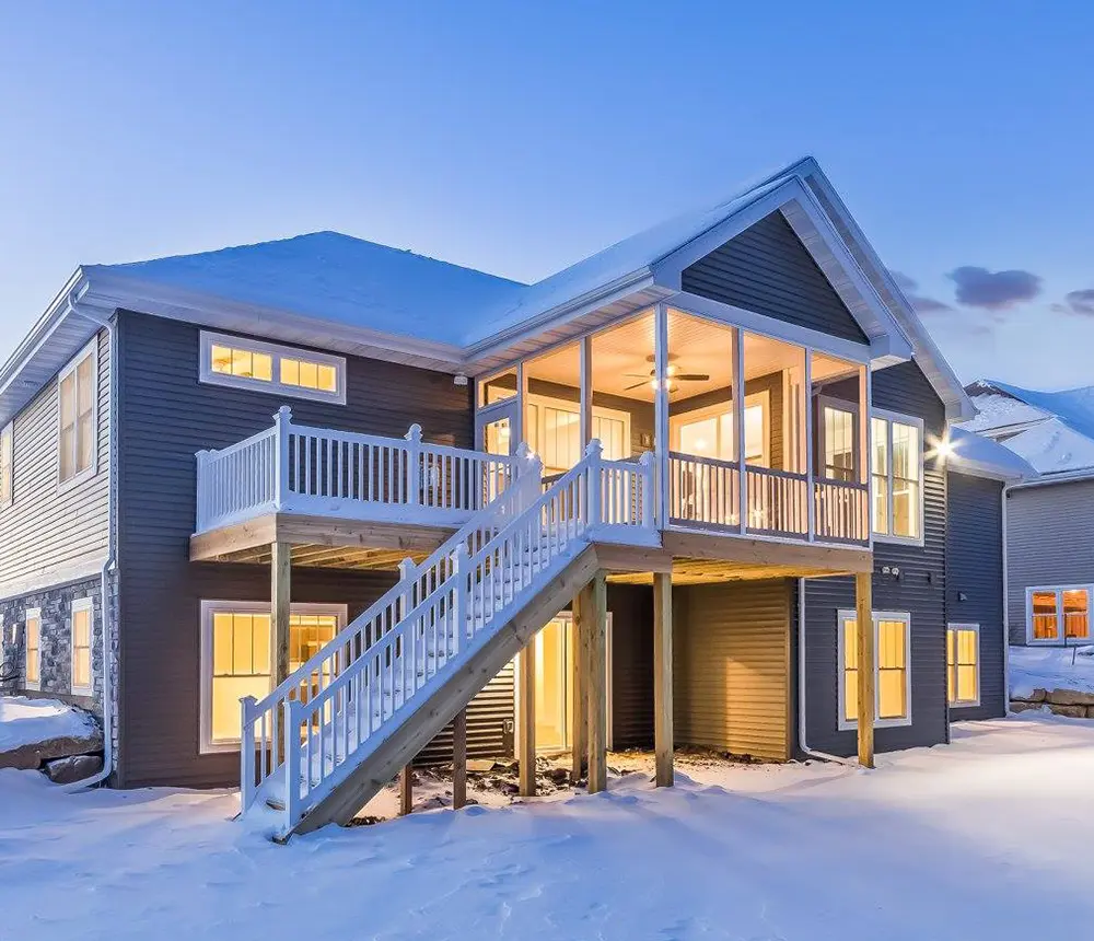 A large home with an elevated pressure treated deck with white metal railing covered in snow